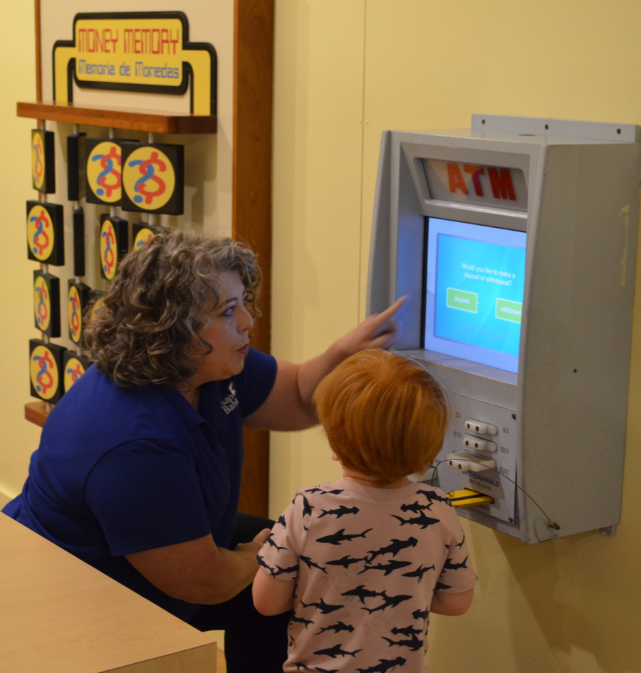 Women showing child a kids play ATM